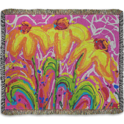 A woven blanket designed with a drip painting of three yellow wildflowers on a pink background, accented by orange, blue, green, and white.
