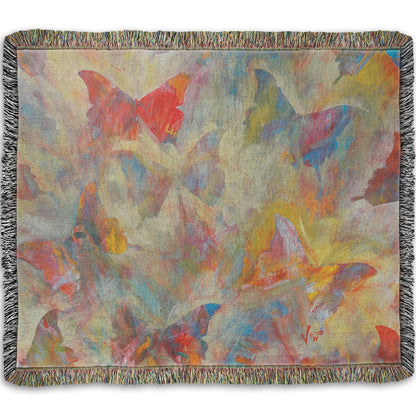 A woven throw blanket designed with an abstracted painting of a pattern of butterflies, created in an array of colors with textured brushstrokes.