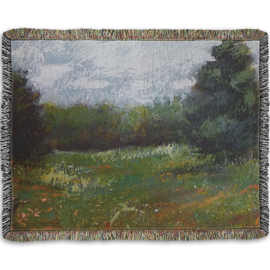 A woven throw blanket designed with an expressive painting of a grassy field and grove of trees.
