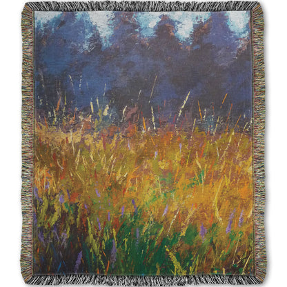 A woven throw blanket designed with an expressive painting of a gold and green field in front of a purple and blue forest.