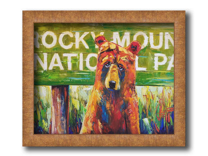 A painting of a bear standing in front of a "Rocky Mountain National Park" sign. Printed on canvas and framed.