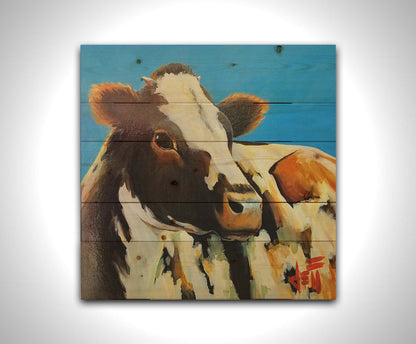 A painting of a cow basking in the sun against a bright blue background. Printed on a wood pallet.