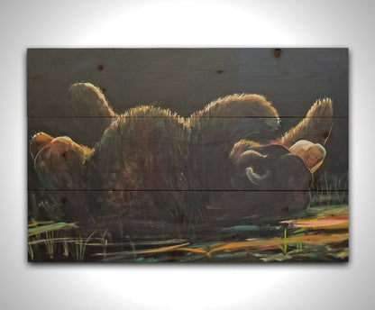 A painting of a bear rolling onto its back, with a dark background. Printed on a wood pallet.