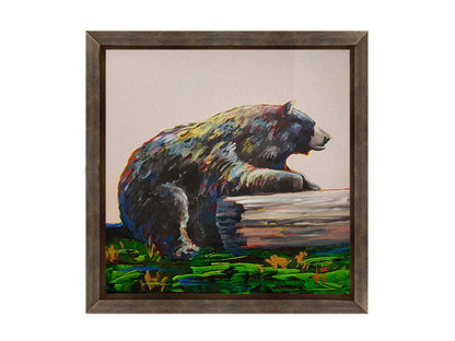 A painting of a bear accented with red, yellow, and blue sitting against a log on bright green grass with a pale pink background. Printed on canvas and framed.