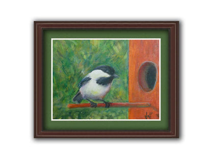 A painting of a black and white chickadee perched on an orange birdhouse, about to enter. The visible brushstrokes of the green background give the impression of foliage. Printed on paper, matted, and framed.