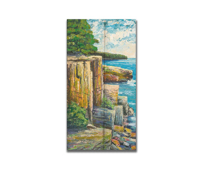 A painting overlooking a waterside clifface. Green forests grow across the tops of the cliffs, and the bright blue waters below splash against a colorful collection of rocks. Printed on a box board.