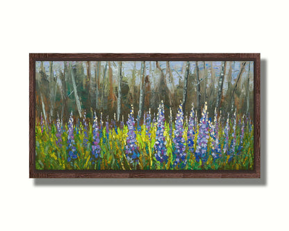 A painting of a field of blue and purple lupine flowers in a green field, backed by a forest. Printed on canvas in a float frame.