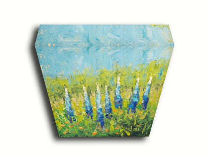 An impasto painting of blue lupine flowers in a green field, complimented by small orange flowers. Printed on canvas.