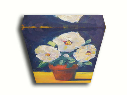 A painting of three white flowers in an orange clay pot. It is sitting on a yellow surface against a dark blue bathroom. Printed on canvas.