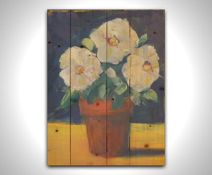 A painting of three white flowers in an orange clay pot. It is sitting on a yellow surface against a dark blue bathroom. Printed on a wood pallet.