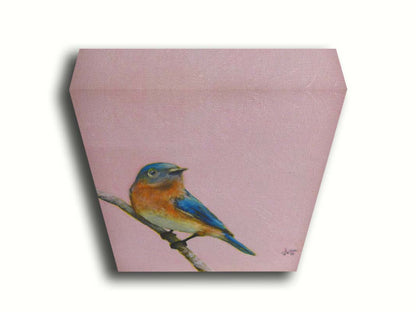 A portrait painting of an eastern bluebird with blue and orange feathers, delicately perched on a twig against a dusty rose pink background. Printed on canvas.