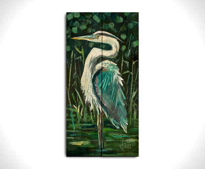 A painting of a great blue heron standing tall in a pond surrounded by vibrant foliage. Printed on a wood pallet.