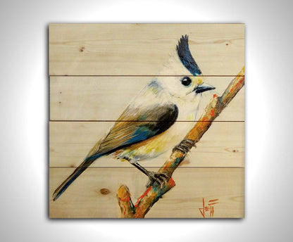 A painting of a titmouse bird with white, yellow, and gray feathers accented with blue perched on a stick, set against an off-white background. Printed on a wood pallet.