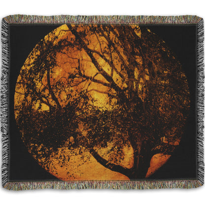 A woven throw blanket designed with a photo of the black shadow of a tree superimposed over a bright orange full moon.