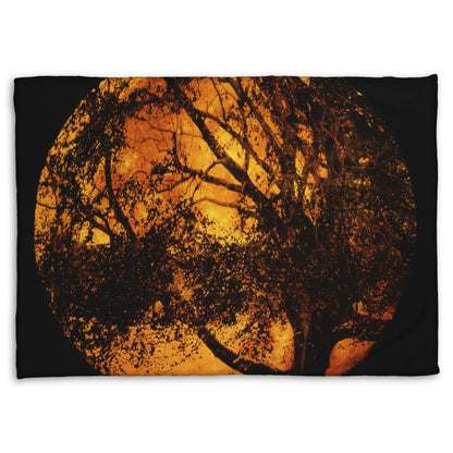 A coral fleece blanket designed with a photo of the black shadow of a tree superimposed over a bright orange full moon.