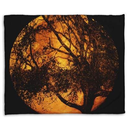 A coral fleece blanket designed with a photo of the black shadow of a tree superimposed over a bright orange full moon.