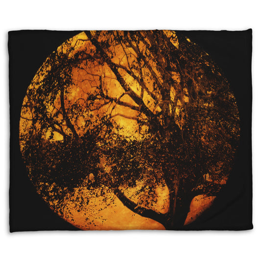 A coral fleece blanket designed with a photo of the black shadow of a tree superimposed over a bright orange full moon.