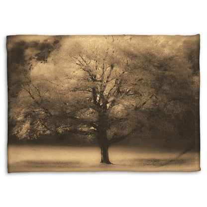 A coral fleece blanket designed with an edited photo of a large, isolated tree in fall, colored in sepia tone.