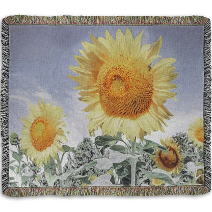 A woven throw blanket designed with a desaturated photo of a group of yellow sunflowers against a blue sky. 