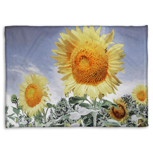 A fleece throw blanket designed with a desaturated photo of a group of yellow sunflowers against a blue sky. 
