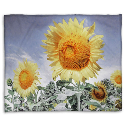 A fleece throw blanket designed with a desaturated photo of a group of yellow sunflowers against a blue sky. 