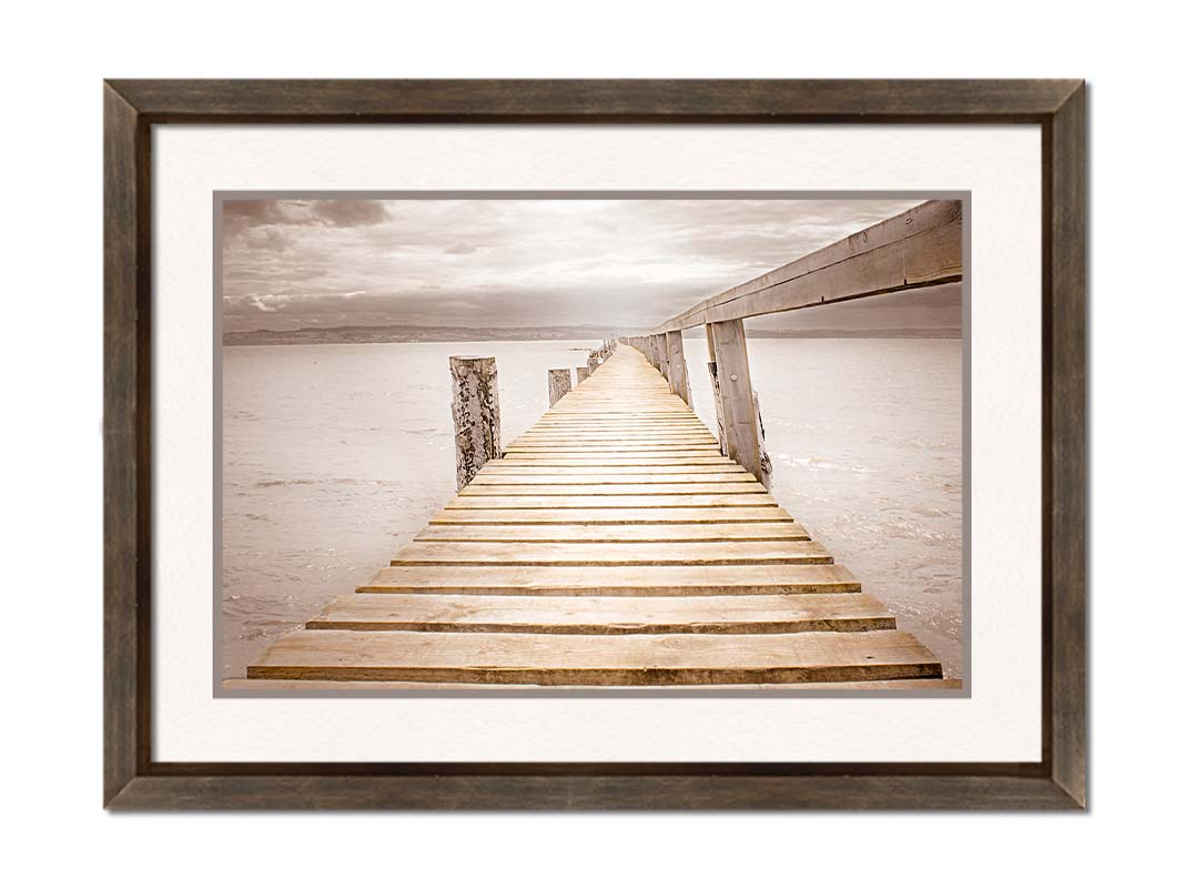 A photo looking along a pier out into the water, edited in a sepia tone. Printed on paper, matted, and framed.