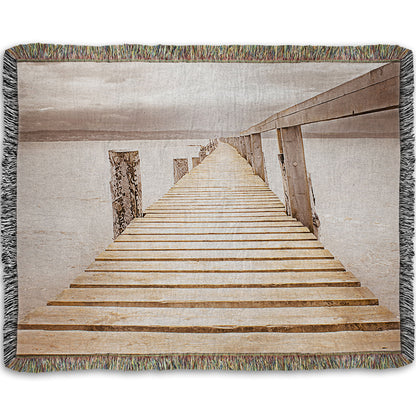 A woven throw blanket designed with a photo looking along a pier out into the water, edited in a sepia tone.