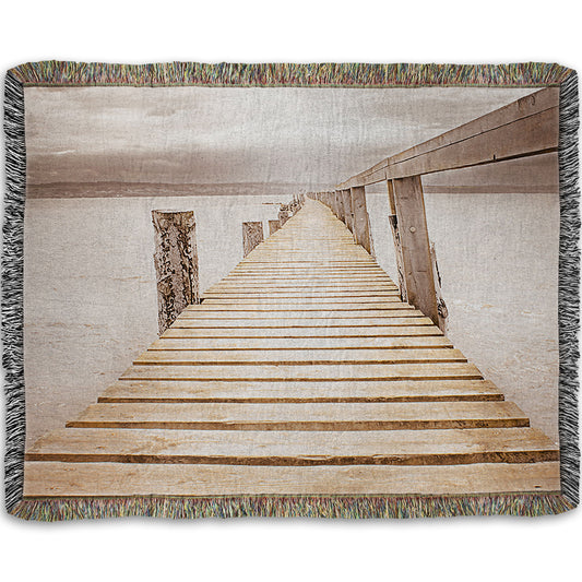 A woven throw blanket designed with a photo looking along a pier out into the water, edited in a sepia tone.