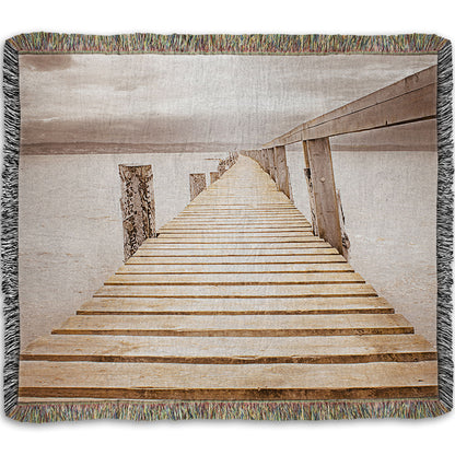 A woven throw blanket designed with a photo looking along a pier out into the water, edited in a sepia tone.