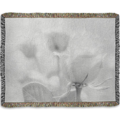 A woven throw blanket designed with a grayscale photo of three roses bathed in a soft white light. 