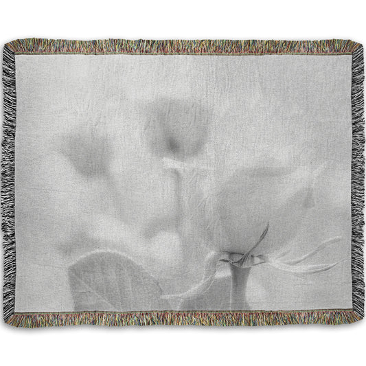 A woven throw blanket designed with a grayscale photo of three roses bathed in a soft white light. 