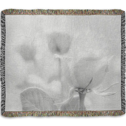A woven throw blanket designed with a grayscale photo of three roses bathed in a soft white light. 