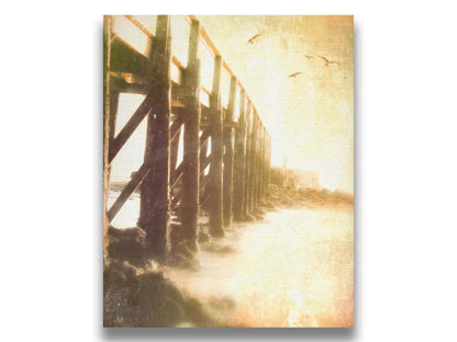 A sepia photo looking out to sea along the side of a pier, as seagulls fly above. Printed on canvas.