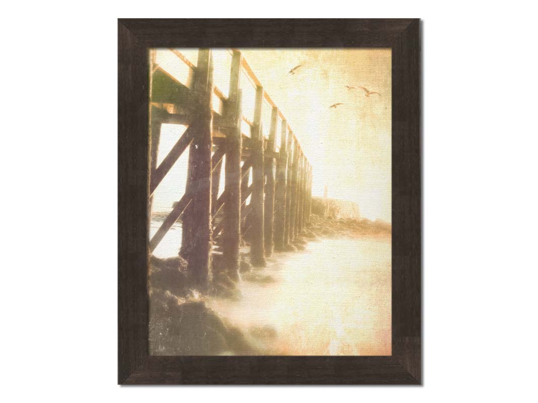 A sepia photo looking out to sea along the side of a pier, as seagulls fly above. Printed on canvas and framed.