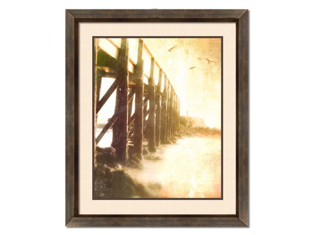 A sepia photo looking out to sea along the side of a pier, as seagulls fly above. Printed on paper, matted, and framed.