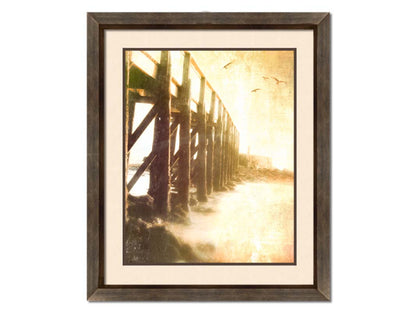 A sepia photo looking out to sea along the side of a pier, as seagulls fly above. Printed on paper, matted, and framed.