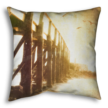 A throw pillow designed with a sepia photo looking out to sea along the side of a pier, as seagulls fly above. 