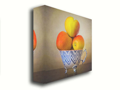 A photograph of a cup full of red and yellow apples, set against a brown table and lighter wall. Printed on canvas.