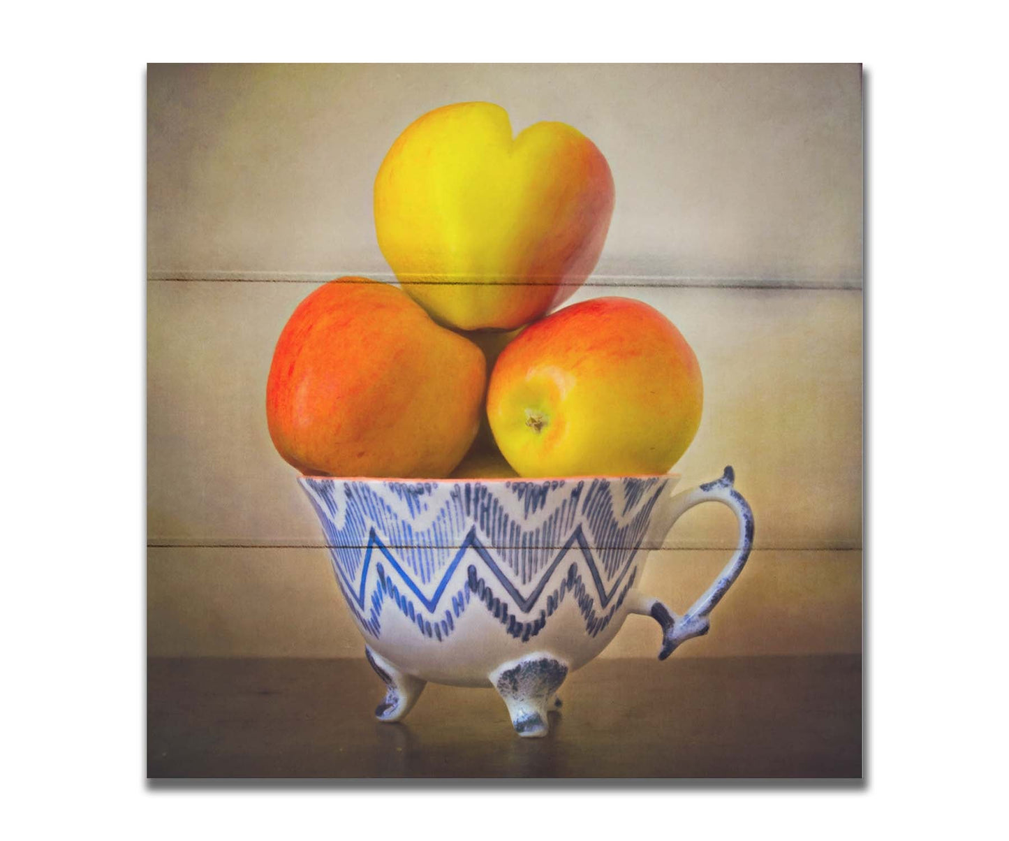 A photograph of a cup full of red and yellow apples, set against a brown table and lighter wall. Printed on a box board.