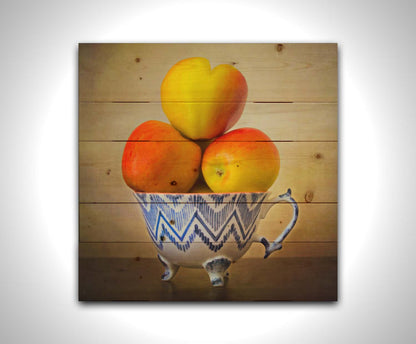 A photograph of a cup full of red and yellow apples, set against a brown table and lighter wall. Printed on a wood pallet.