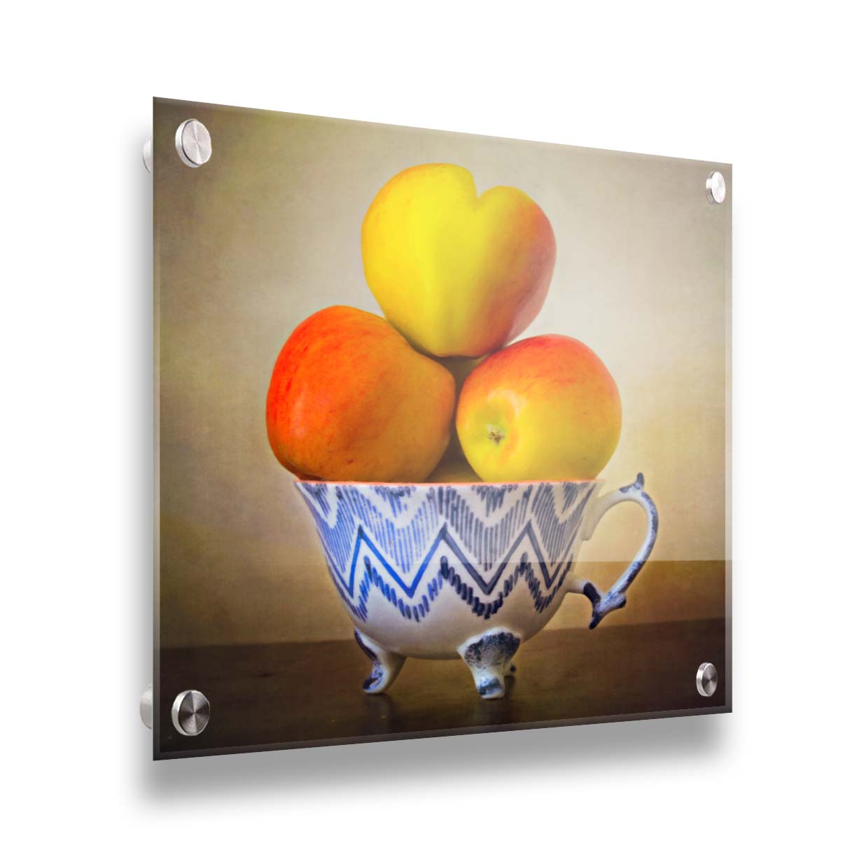 A photograph of a cup full of red and yellow apples, set against a brown table and lighter wall. Printed on acrylic.