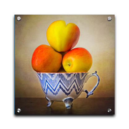 A photograph of a cup full of red and yellow apples, set against a brown table and lighter wall. Printed on acrylic.