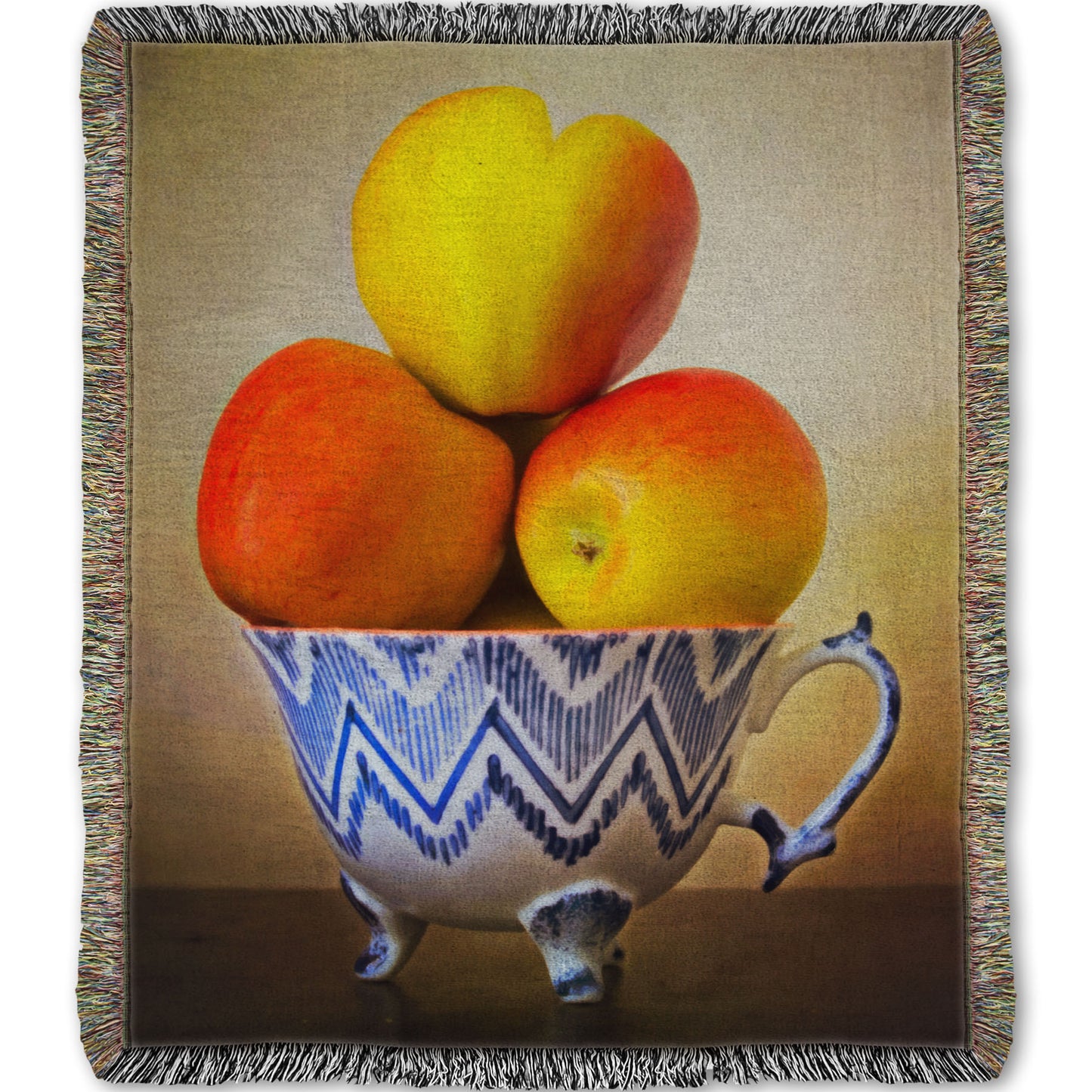 A woven blanket designed with a photograph of a cup full of red and yellow apples, set against a brown table and lighter wall. 