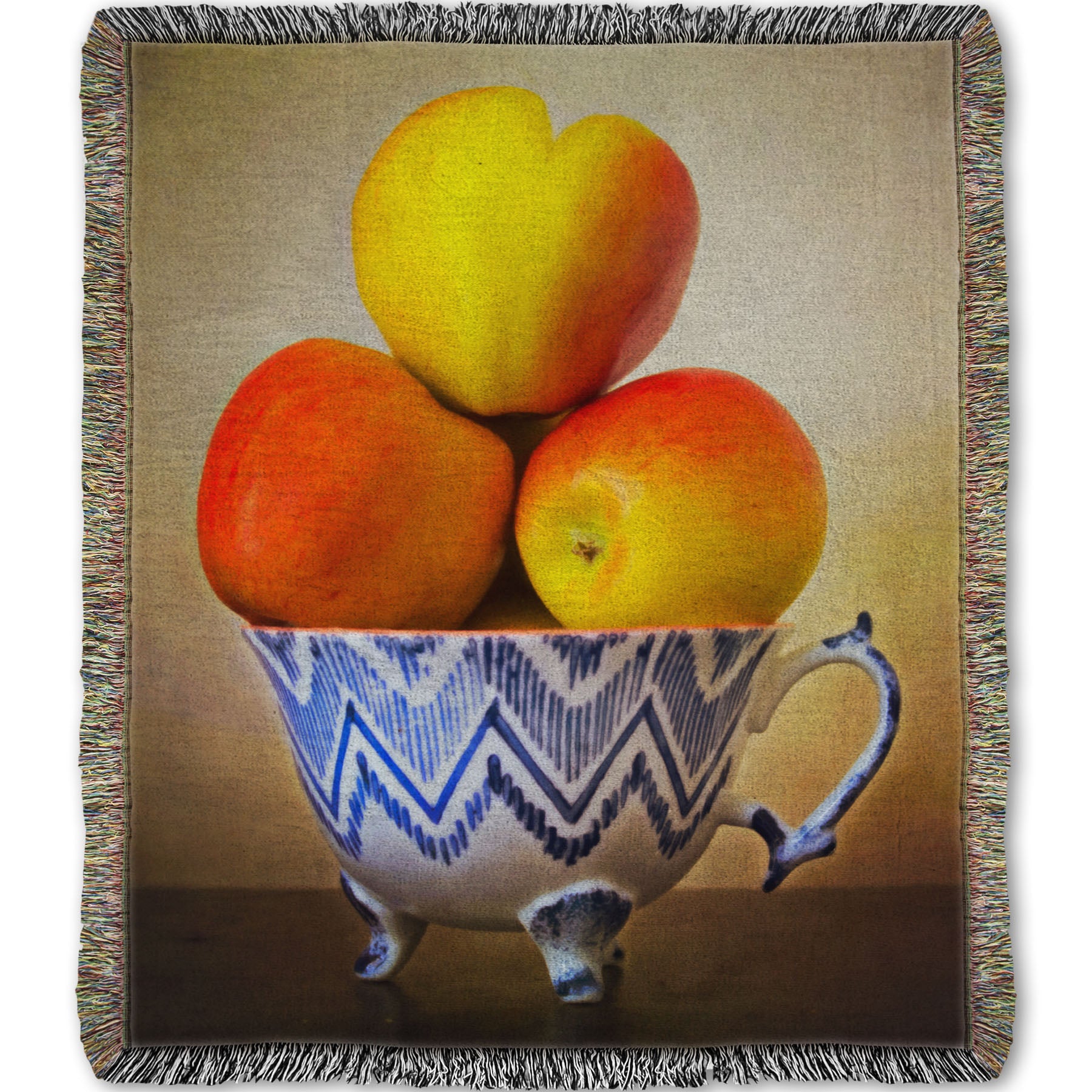 A woven blanket designed with a photograph of a cup full of red and yellow apples, set against a brown table and lighter wall. 