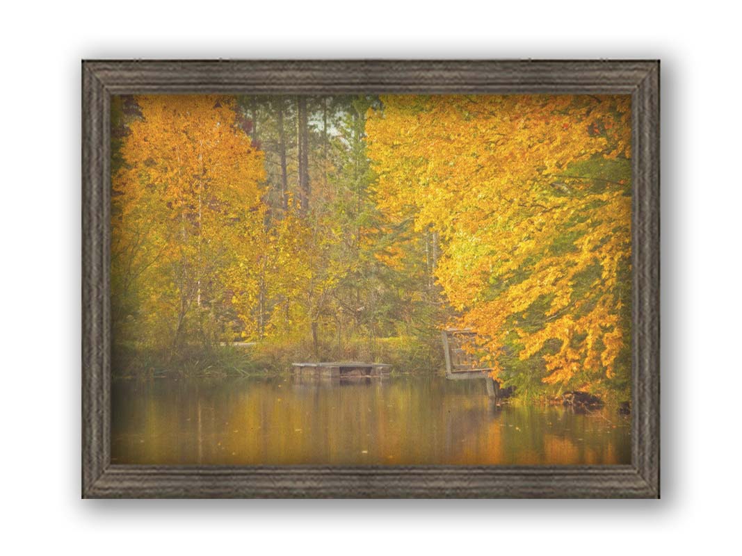 A photo of yellow autumn trees at a pond, their leaves reflecting off the water. Printed on canvas and framed.