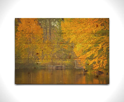 A photo of yellow autumn trees at a pond, their leaves reflecting off the water. Printed on a wood pallet.