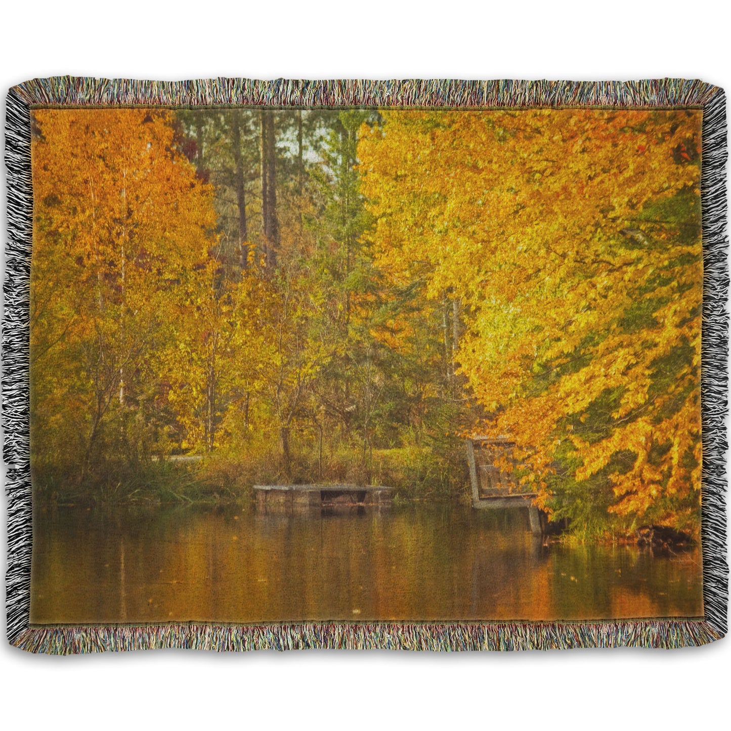 A woven throw blanket designed with a photo of yellow autumn trees at a pond, their leaves reflecting off the water. 