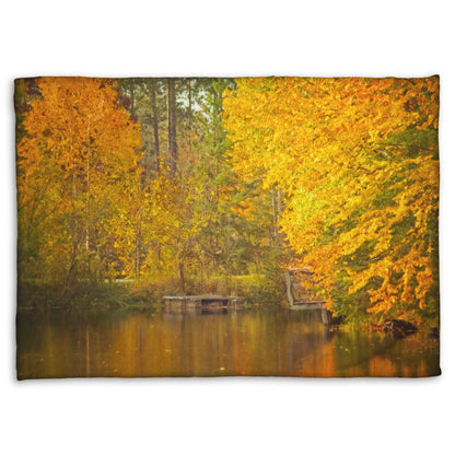 A fleece throw blanket designed with a photo of yellow autumn trees at a pond, their leaves reflecting off the water. 