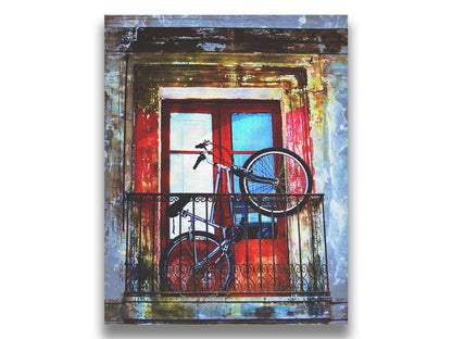 A photo of a bike propped up on a balcony in front of a red door. Printed on canvas.