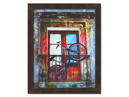 A photo of a bike propped up on a balcony in front of a red door. Printed on canvas and framed.